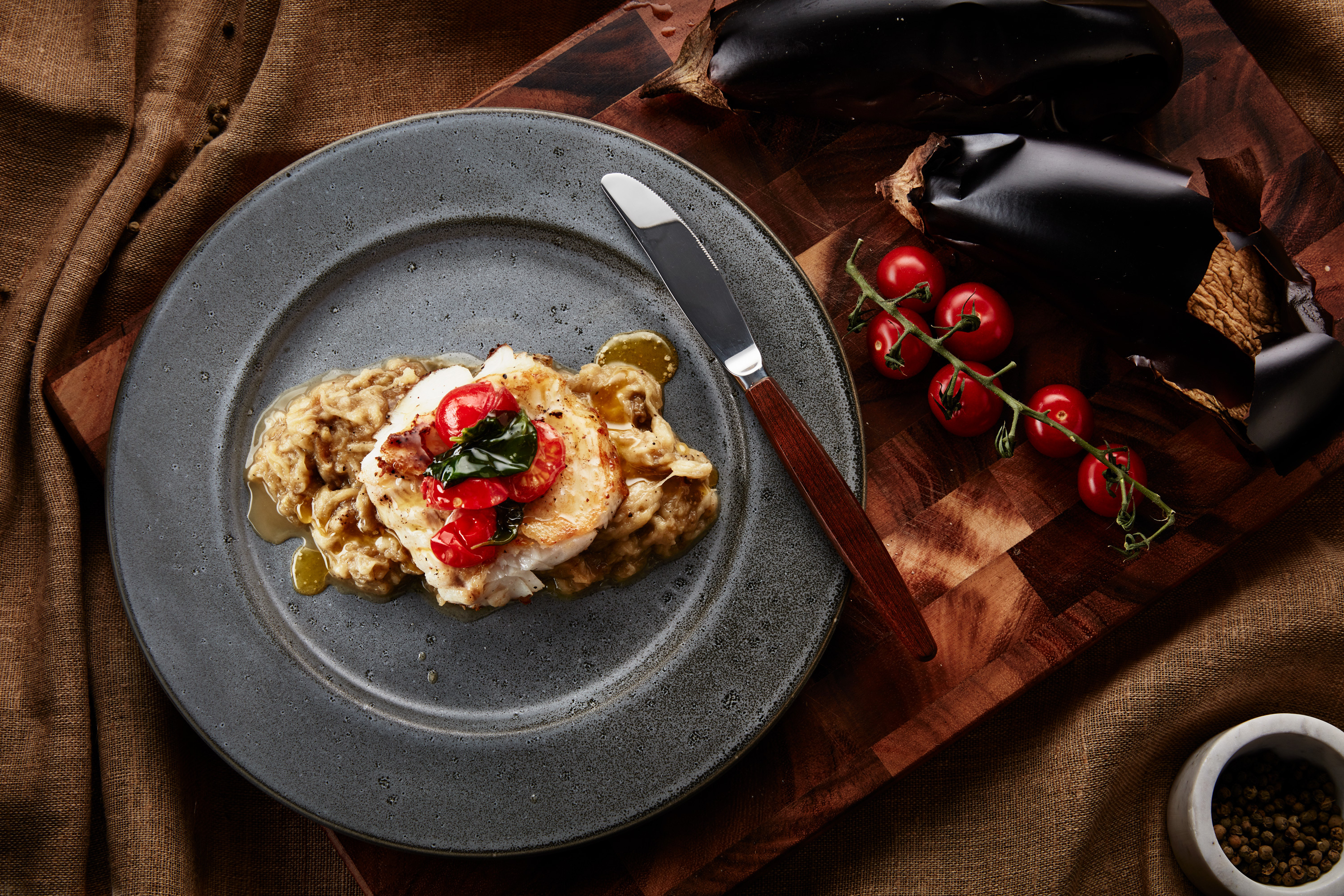 Tallerken på et bord med stekt skrei med basilikumsmør og tomater