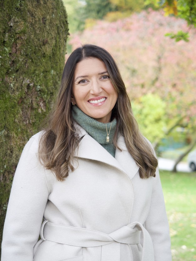 Kvinne som smiler til kameria med natur i bakgrunnen