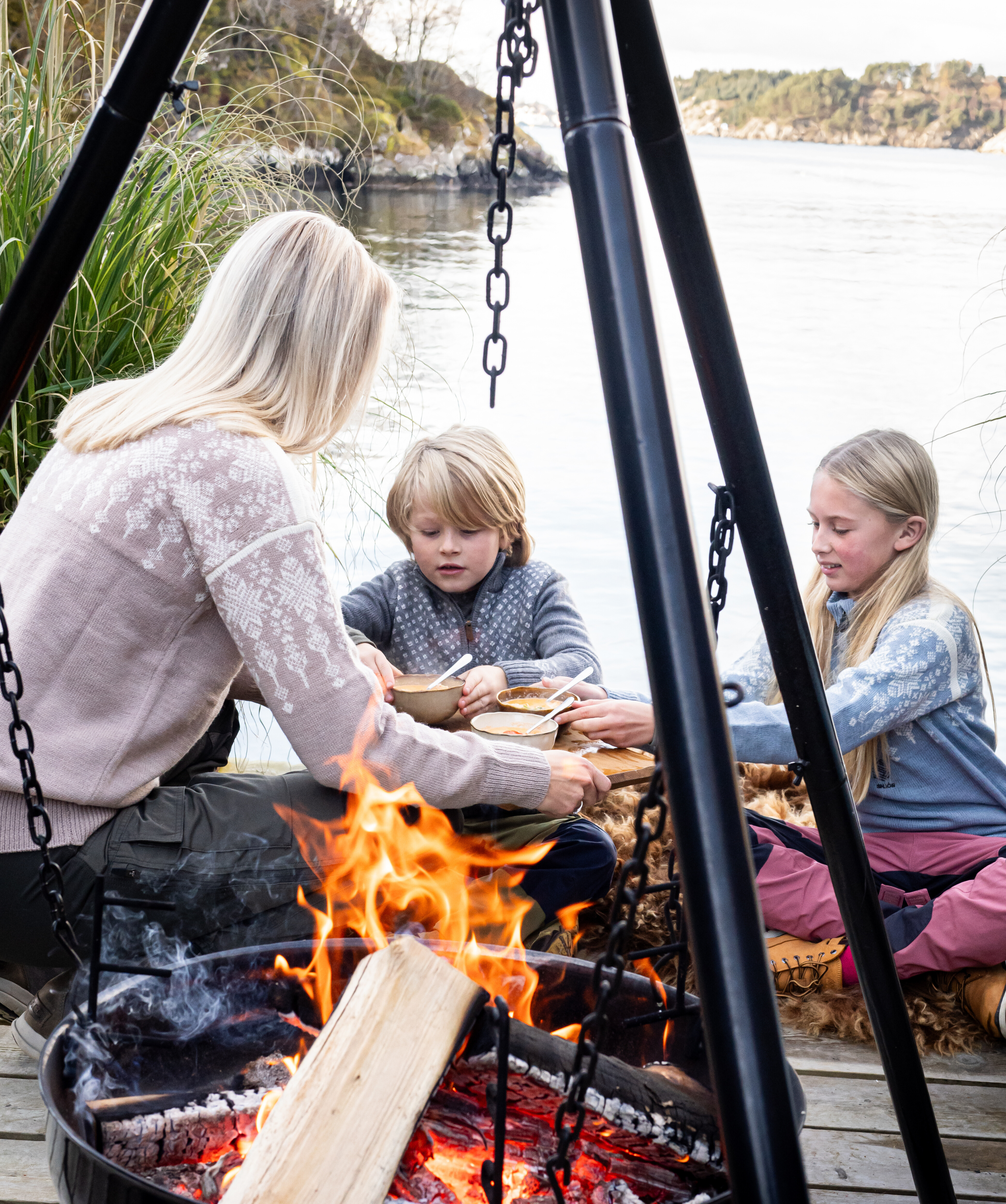 Barn og mor rundt et bål med skåler med fiskesuppe