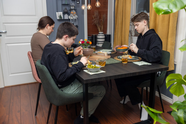 Kvinne med to tenåringer sitter rundt et bord. På bordet er det middag og tilbehør.